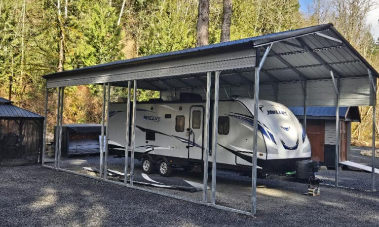 RV parked under metal carport with trees in background.