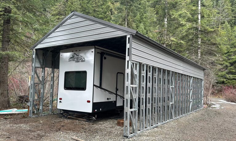 RV under metal carport in forested area.
