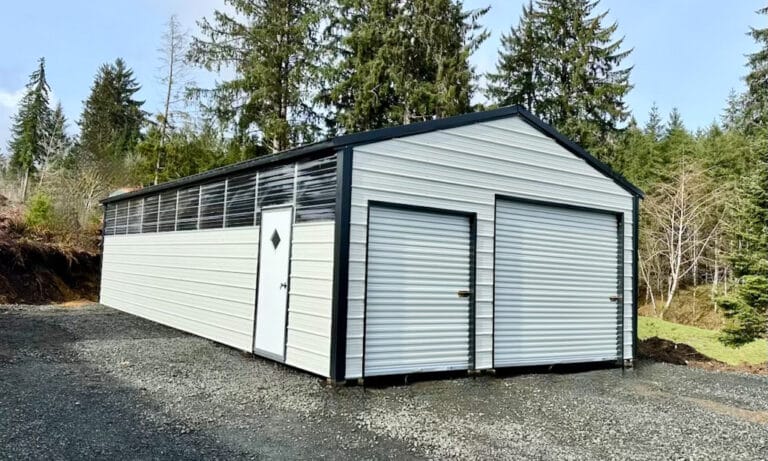 Large white metal barn with forest backdrop.