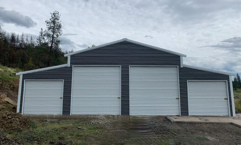 Large metal garage with three doors in forest.